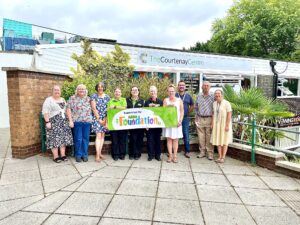 Asda and Courtenay Centre staff stand outside the community centre holding a banner to celebrate the new funding